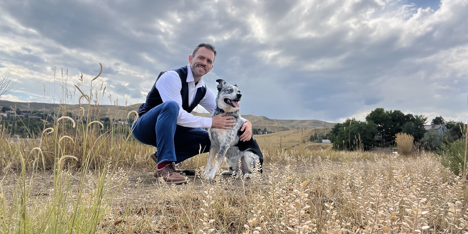 maveriQ B Jackson crouching beside his dog in the Colorado foothills
